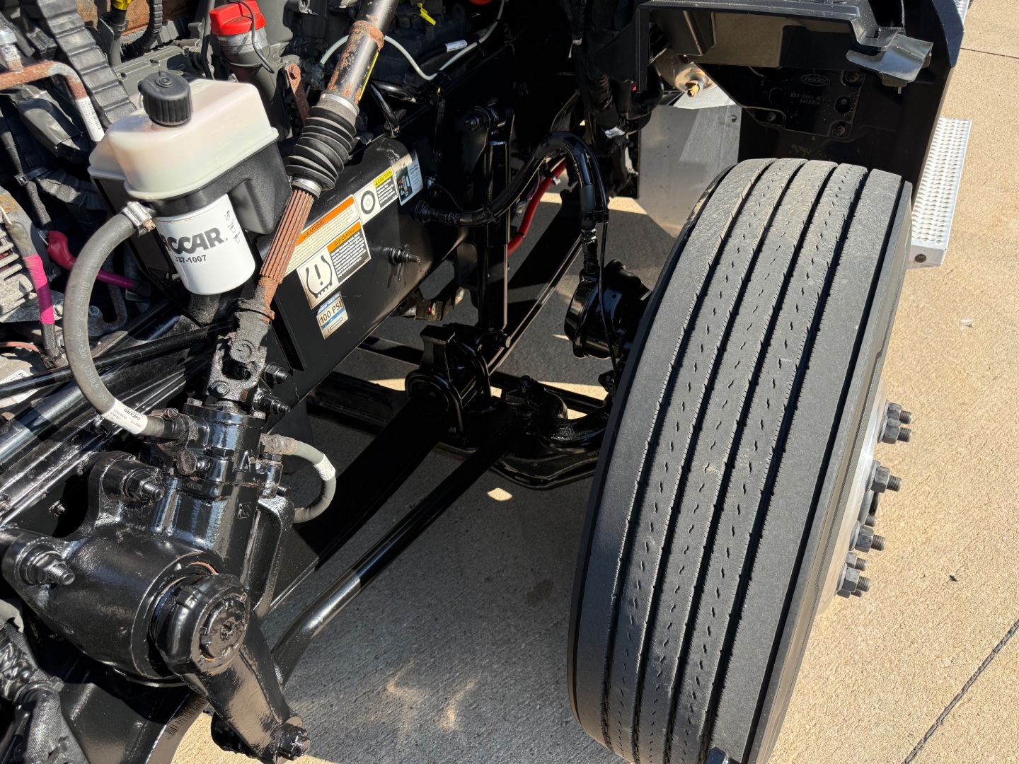 Peterbilt 579 truck engine bay and front dual wheels showing coolant reservoir, hydraulic lines, and steering components.