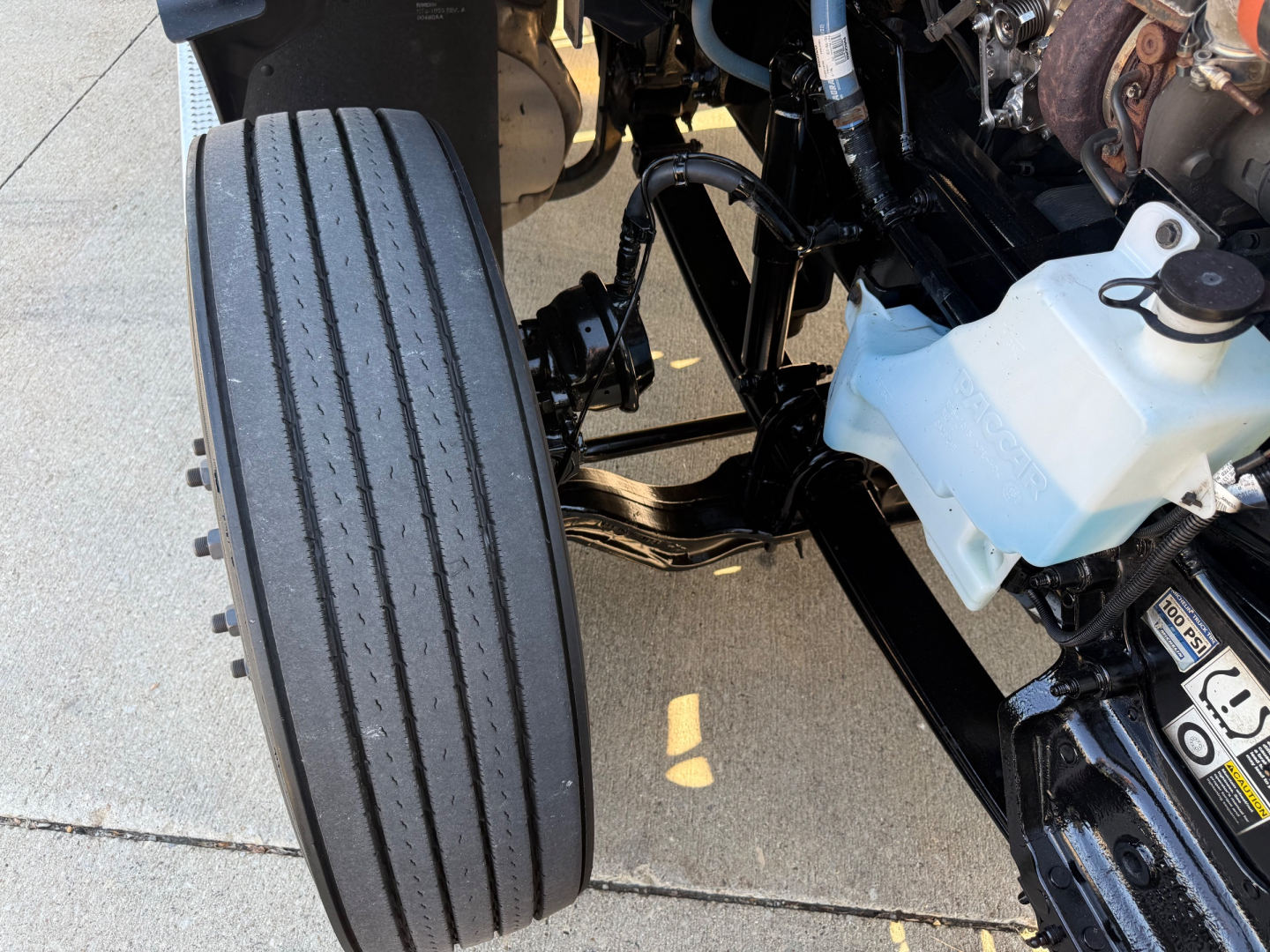 Peterbilt 579 front wheel and engine bay area showing black frame, coolant reservoir, and brake lines.