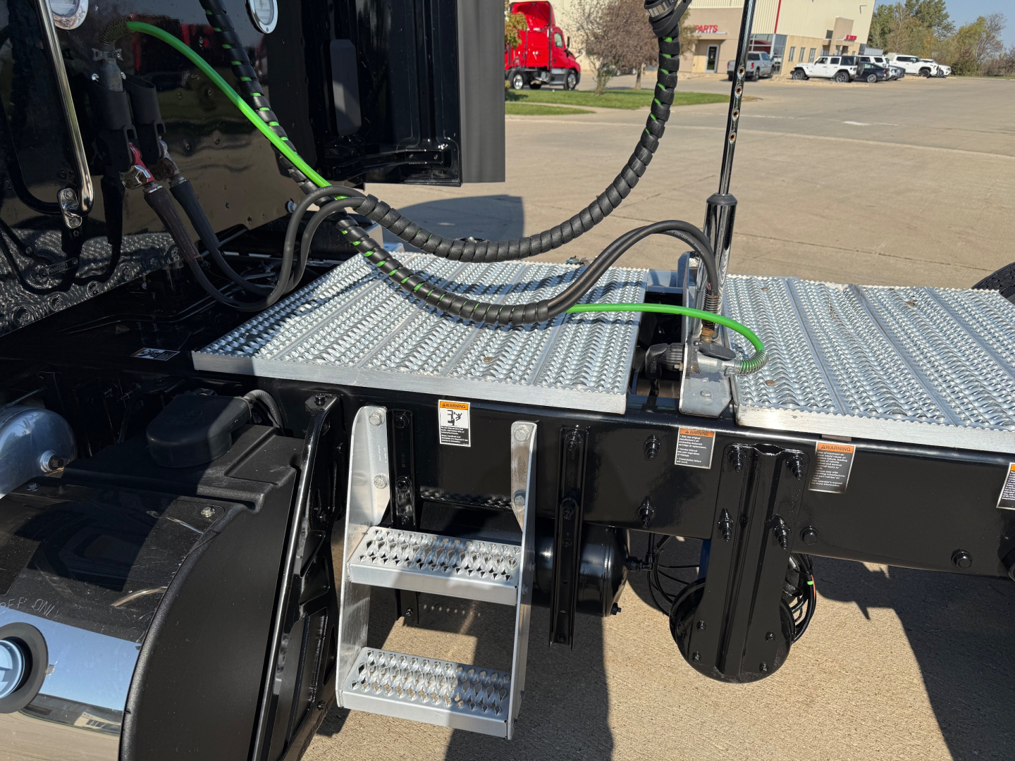 Peterbilt 579 cab area with aluminum diamond-plate step/landing and hydraulic lines; visible steps and platform near the driver side, electrical cables, and components.