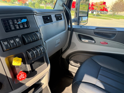 Peterbilt 579 truck cabin interior showing dashboard switches, air vents, ignition area, and passenger door with badge.