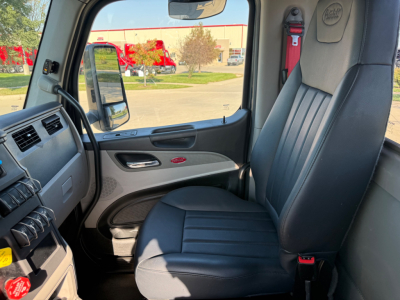 Peterbilt 579 cab interior showing driver seat and dashboard with door panel and window; view through passenger side window.