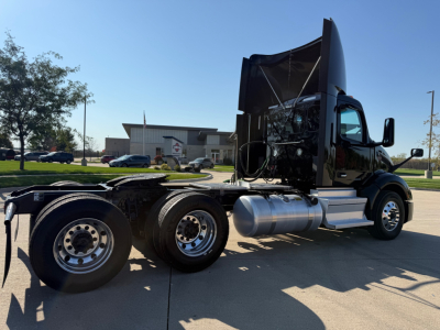 Peterbilt 579 daycab tractor with hood raised, showing engine area and side tanks, triple-axle rear with aluminum fuel tanks.