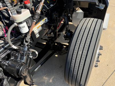 Peterbilt 579 truck engine bay and front dual wheels showing coolant reservoir, hydraulic lines, and steering components.