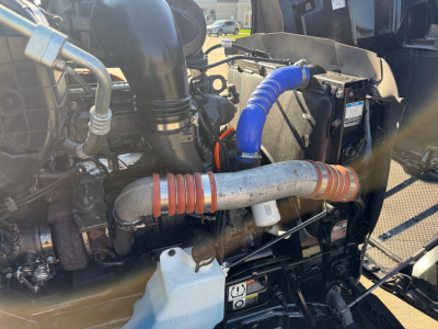 Peterbilt 579 engine bay with visible intercooler piping and hoses, blue radiator hose, white coolant reservoir cap, and surrounding components.