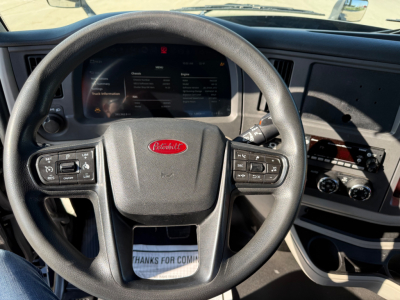 Peterbilt truck dashboard with steering wheel and instrument cluster; center shows Peterbilt emblem on wheel; displays digital screen with vehicle info; controls on steering wheel and dashboard gauges visible.