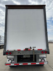 Trailer rear showing white cargo area with metal frame and taillights, rear bumper, and latching mechanism.