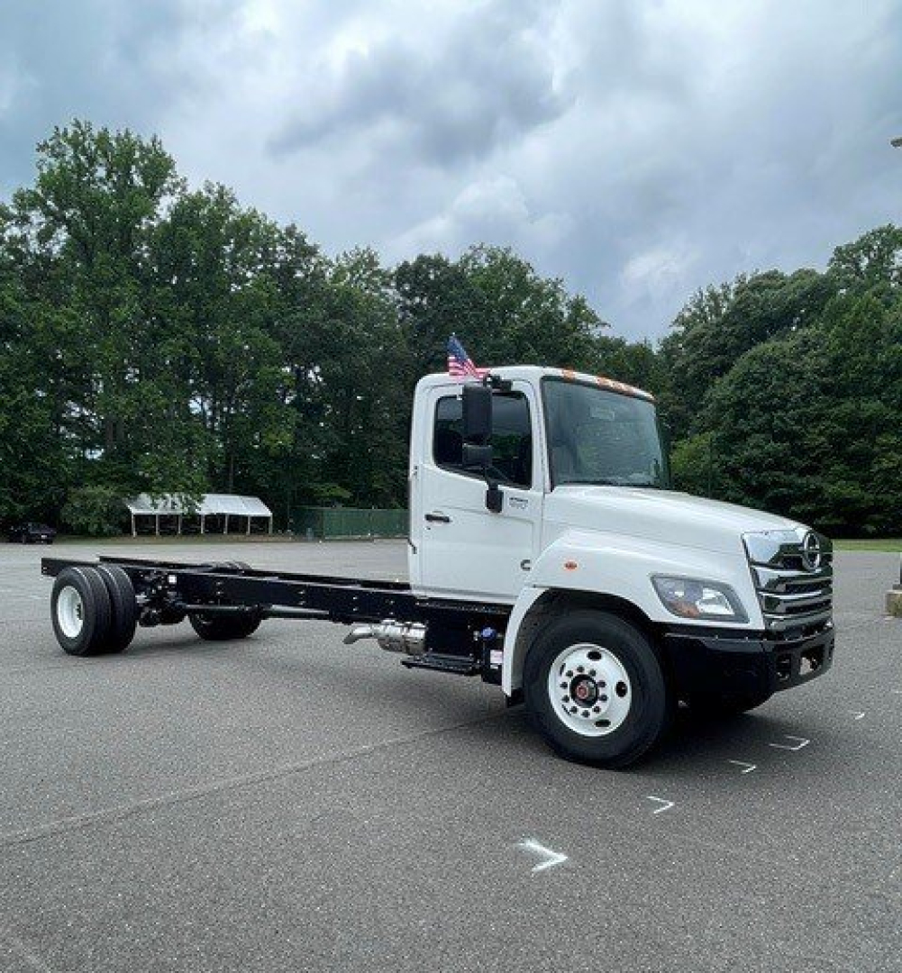 White Hino L7 cab chassis truck with flatbed chassis, front grille with chrome, American flag on cab, in a parking lot.