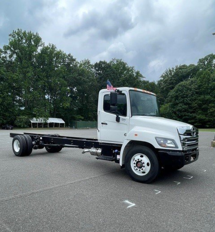 White Hino L7 cab chassis truck with flatbed chassis, front grille with chrome, American flag on cab, in a parking lot.