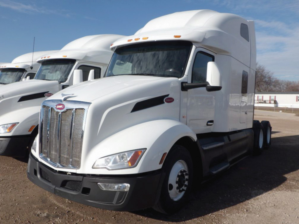 Peterbilt 579 sleeper tractor in white, front three-quarter view, chrome grille, large aerodynamic hood, dual rear axles, side steps, daytime running lights.