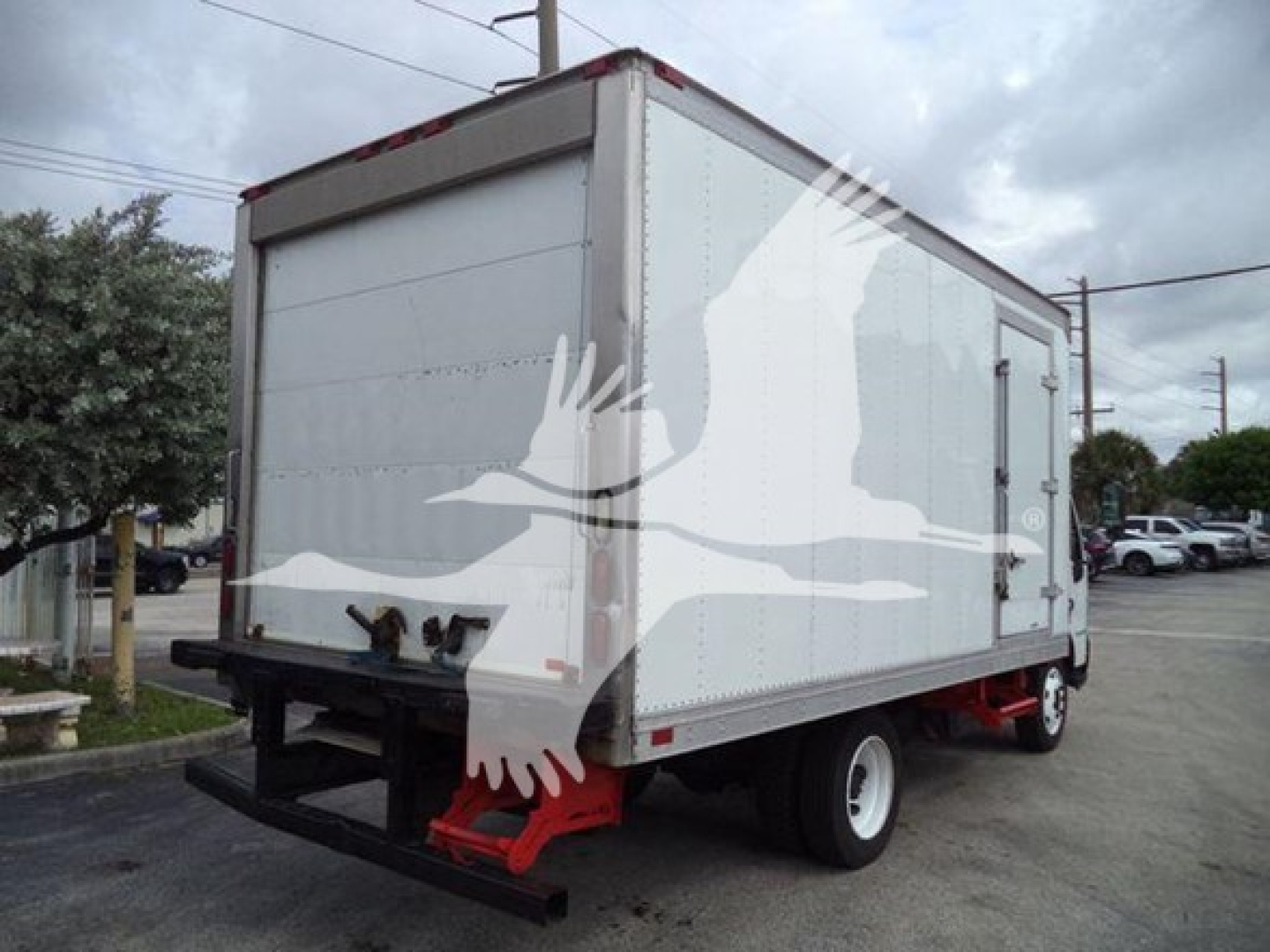 Box truck with white refrigerated body and black underride bumper, rear view showing red suspension components and dual rear wheels.