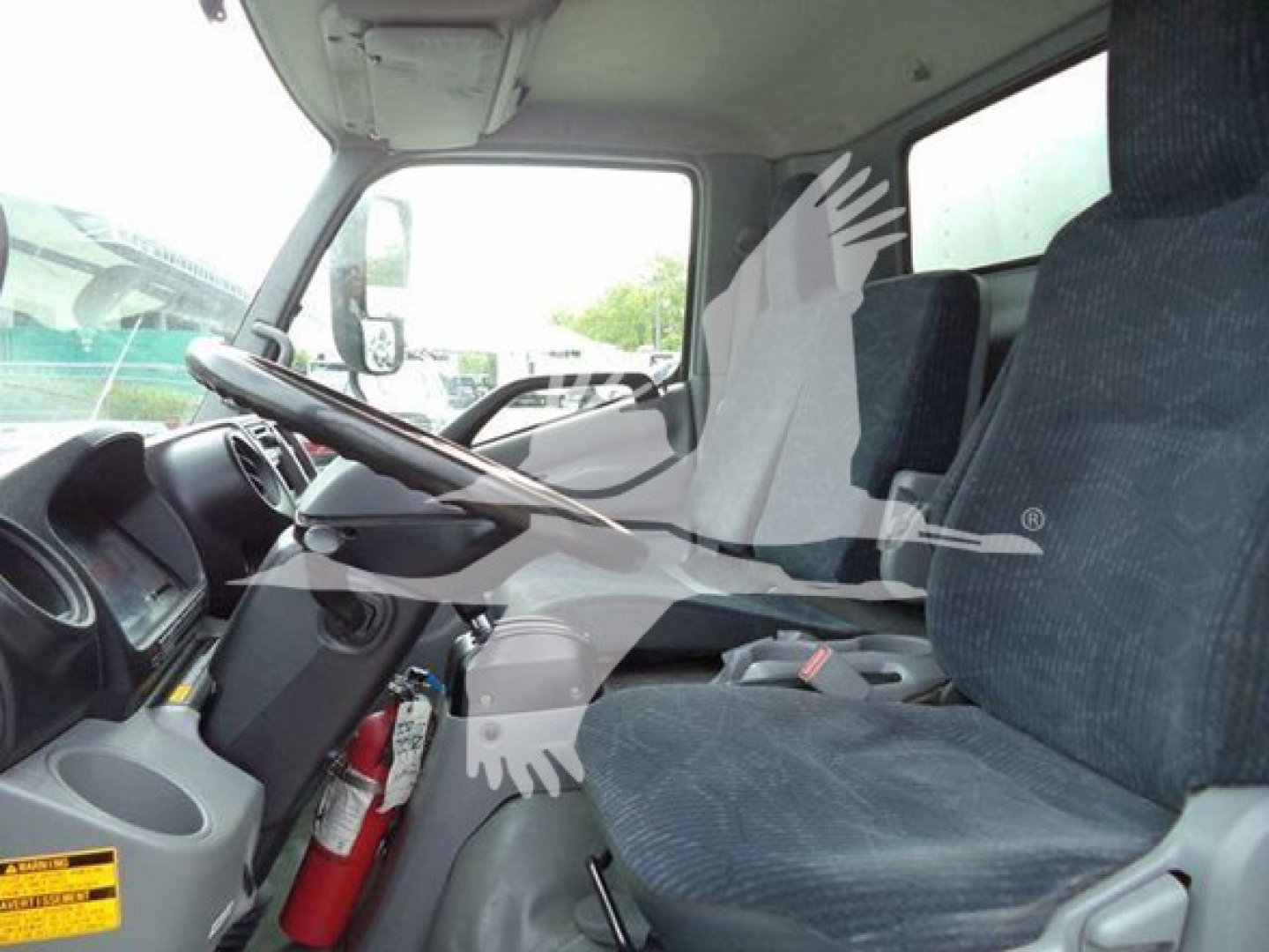 Interior cab view of a 2019 Hino 195 refrigerated truck showing steering wheel, driver and passenger seats, dash controls, and a fire extinguisher mounted beside the seat.