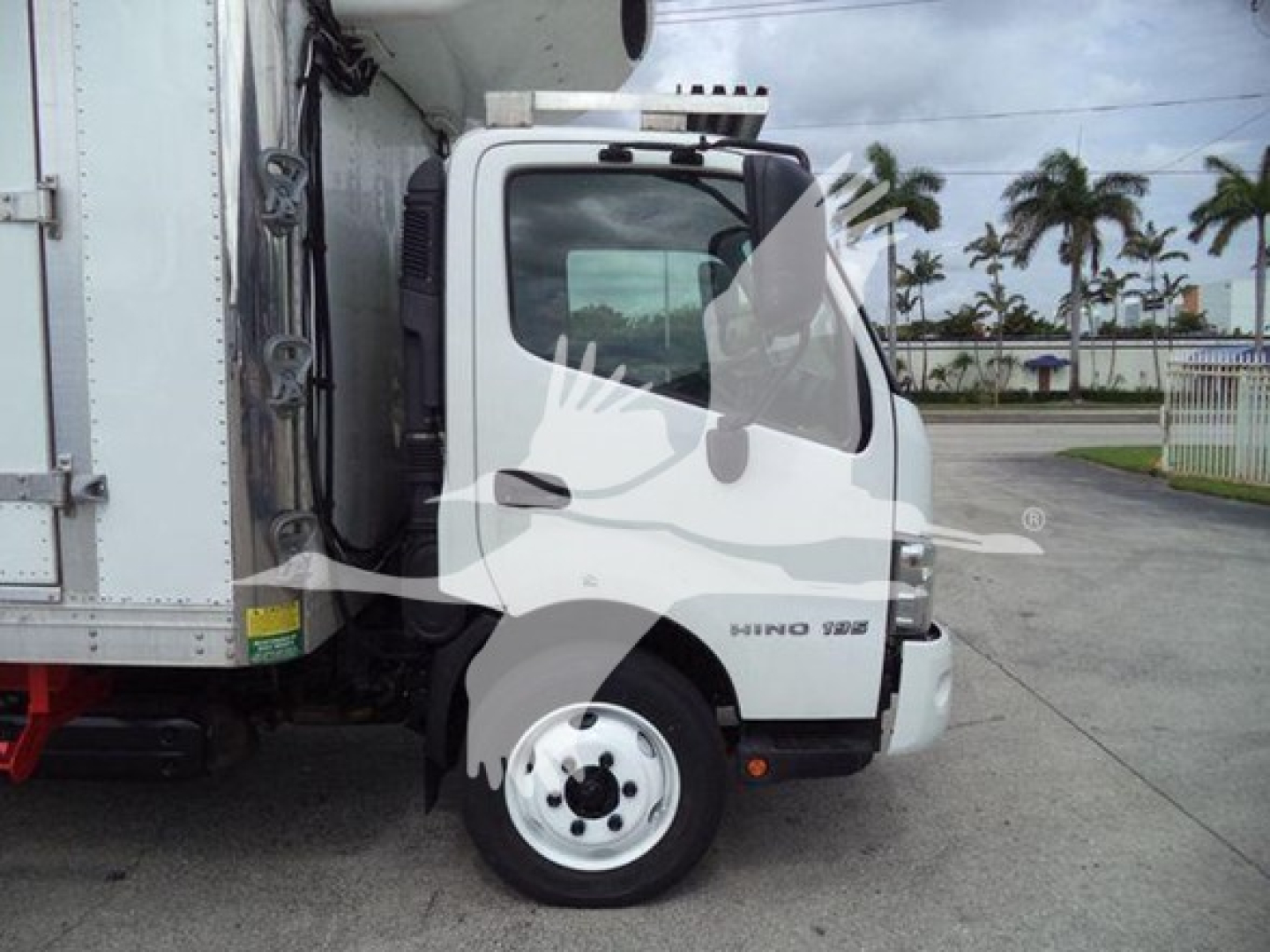 Side view of a 2019 Hino 195 refrigerated truck cab with white exterior and black front grille, showing the cab door, front wheel, and portion of the refrigerated box.