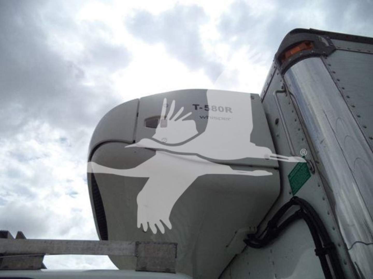 Refrigerated truck cab area showing a Thermo King T-580R unit mounted on a Hino 195 rooftop, partial trailer with curved corner, cloudy sky
