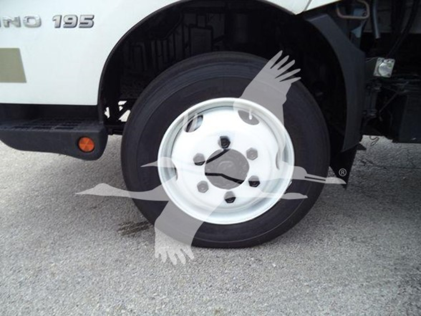 Wheel and fender of a white 2019 Hino 195 refrigerated truck showing front wheel and badge area.