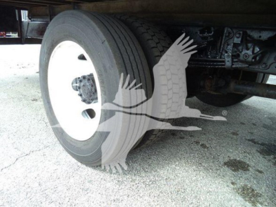 Trailer/vehicle wheel assembly showing dual rear wheel with white steel rim and tire in-view under carriage; parts of suspension and chassis visible.