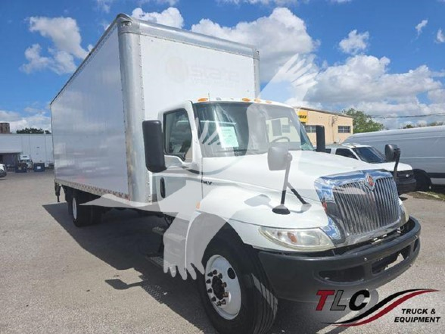 Box truck with white cab and large cargo box in a lot, International logo on grille, stock number and VIN not visible text on side panels.