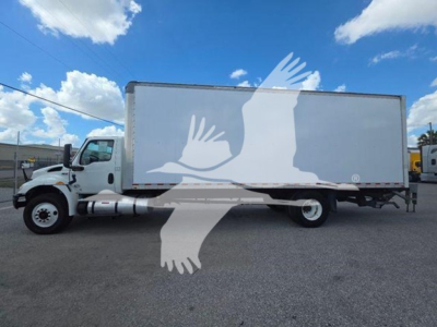 Box truck with white cab and cargo box parked on gravel lot. Side view shows International MV series truck with large white trailer. Clear blue sky with clouds.