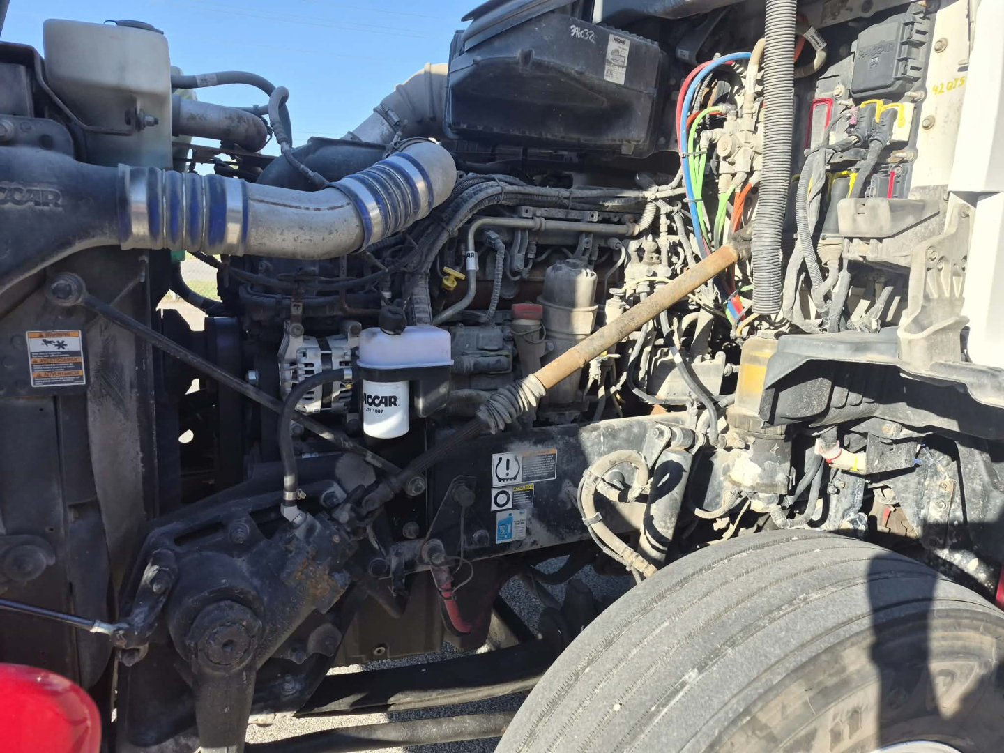 Kenworth T880 engine bay showing various hoses, hoses, battery, and hydraulic components.