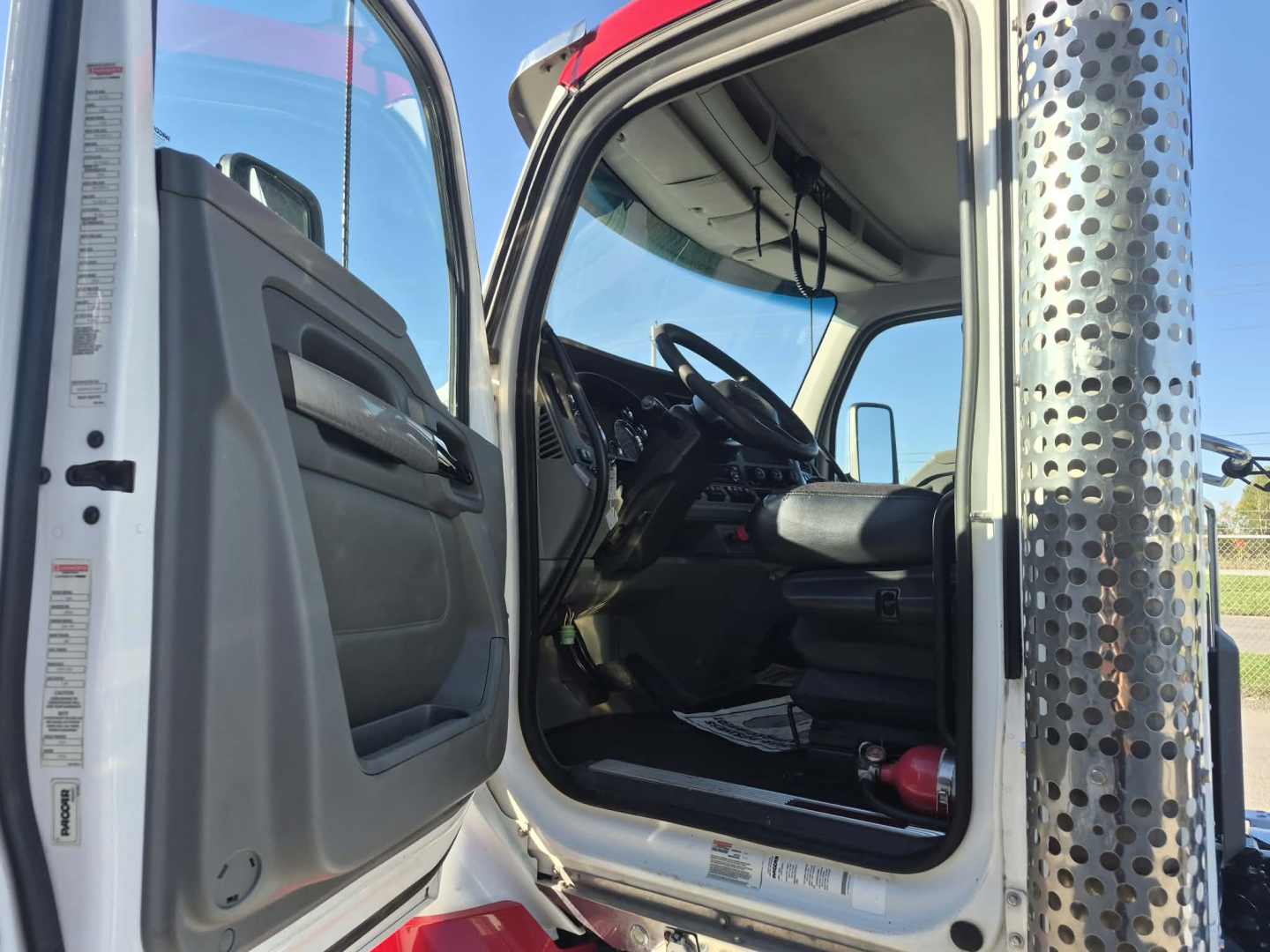 Cab interior of a 2018 Kenworth T880 with open driver door showing steering wheel, dashboard, and seating; exterior chrome exhaust stack visible on right.