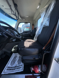 Cab interior of a 2018 Kenworth T880 with black driver seat, steering wheel, and dashboard; plastic seat cover on passenger area and a red fire extinguisher near the door.