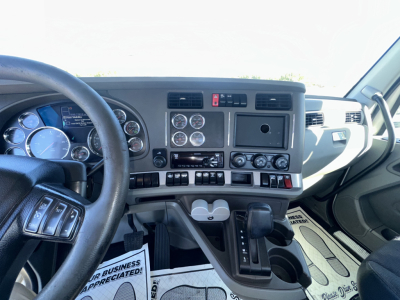 Kenworth truck interior dashboard with multiple gauges, steering wheel, gear shifter, and center console gauges. Text visible includes various gauges and controls but no legible model details beyond general dashboard components.