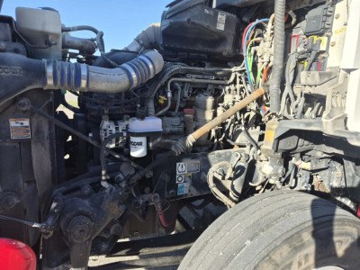 Kenworth T880 engine bay showing various hoses, hoses, battery, and hydraulic components.