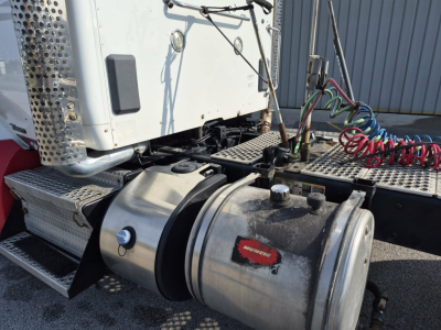 Kenworth T880 tractor engine bay showing fuel tank, air lines, and steps with black hose and metallic components.