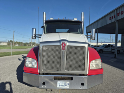 Kenworth T880 conventional daycab front view showing large chrome grille, dual tall exhaust stacks, red fenders, and bumper with license plate.