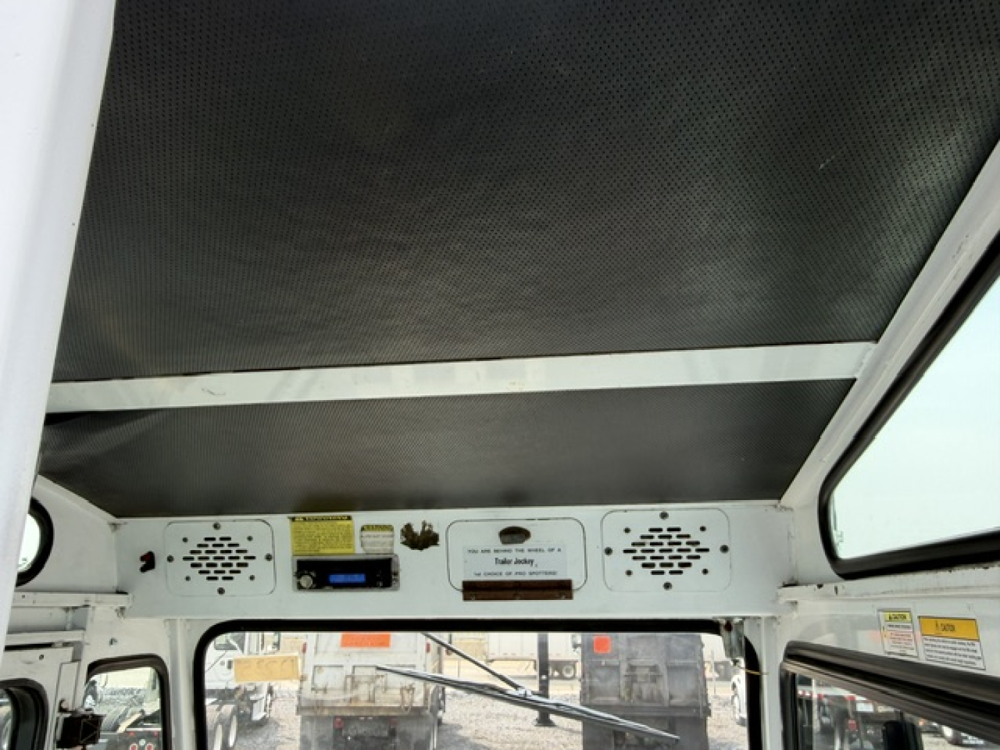 Captionless interior view of a Capacity TJ5000 truck cab, dashboard vents, switches, and overhead ceiling; visible metal framework and side windows.