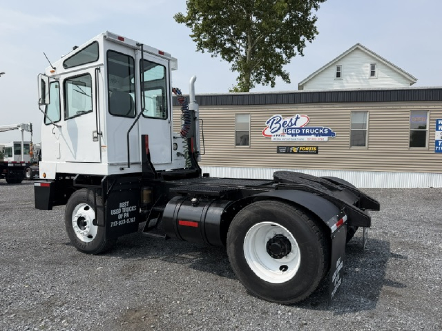 Truck chassis with cab on a yard lot, showing TJ5000 capacity label and dual rear wheels, white cab, side view