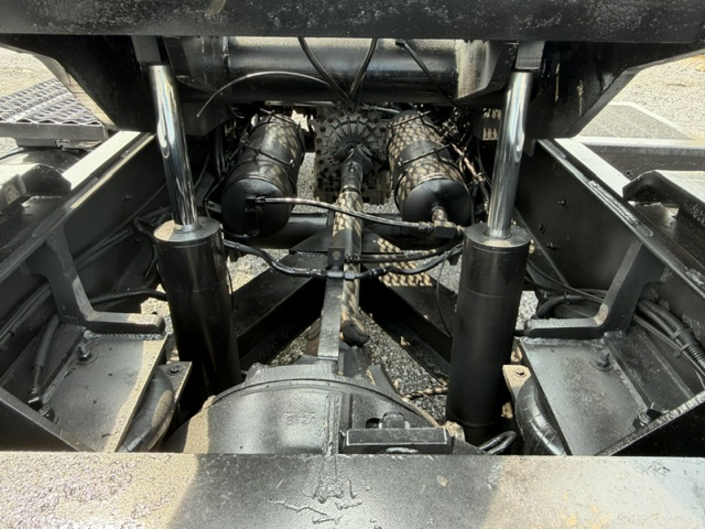 Trucks chassis underside showing dual hydraulic shocks and drivetrain components, hoses, and frame rails; visible pump lines and connectors.