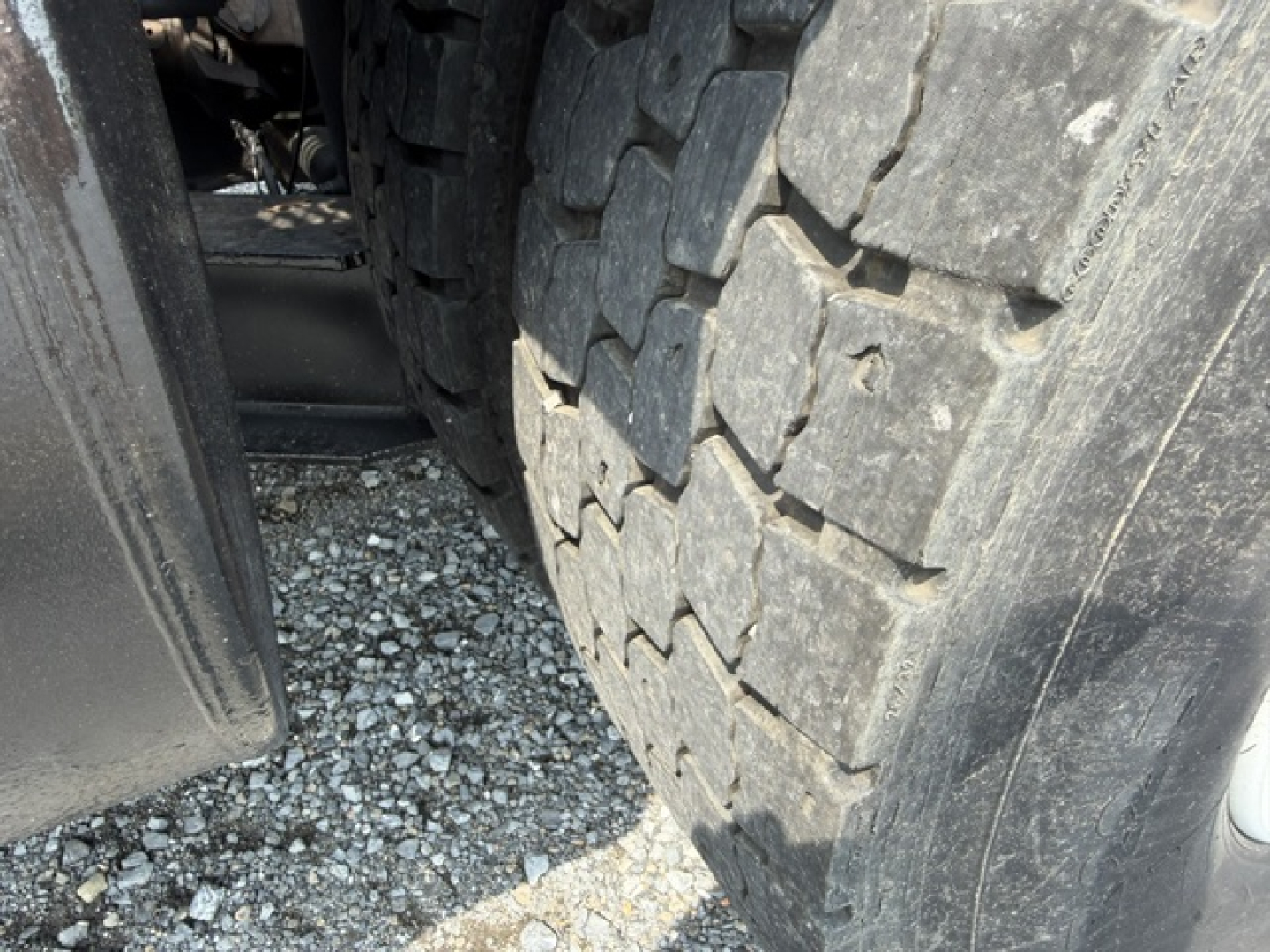 Truck wheel and heavy tread tire close-up view showing part of the chassis and ground surface.