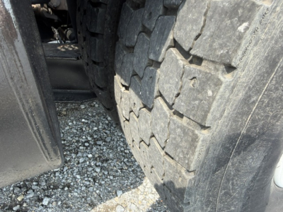 Truck wheel and heavy tread tire close-up view showing part of the chassis and ground surface.