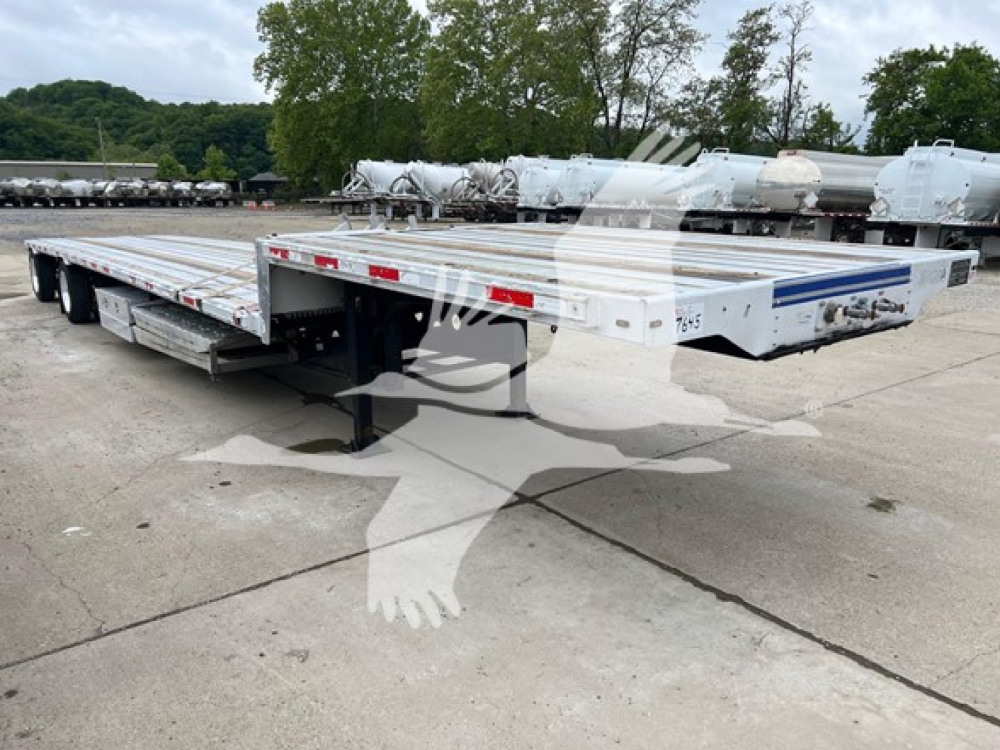 Transcraft D-Eagle II drop deck trailer showing exterior white aluminum deck with blue stripe, rear ramps, and dual axle configuration.