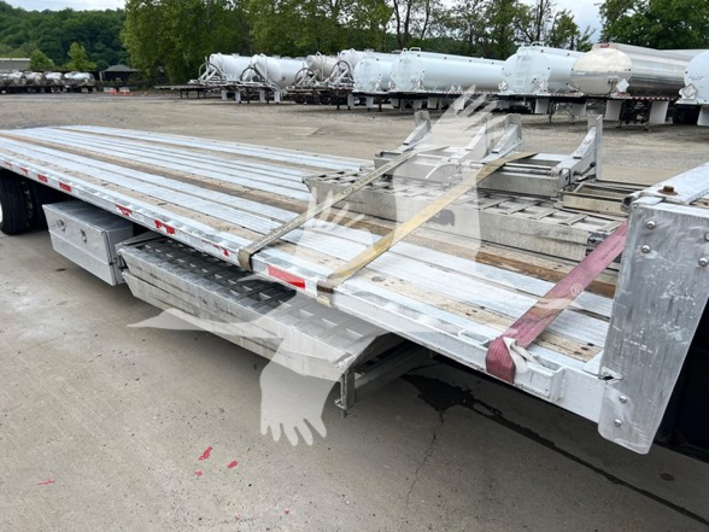Trailer deck with stacked aluminum planks and securing straps, showing edge rails and rear tie-downs.