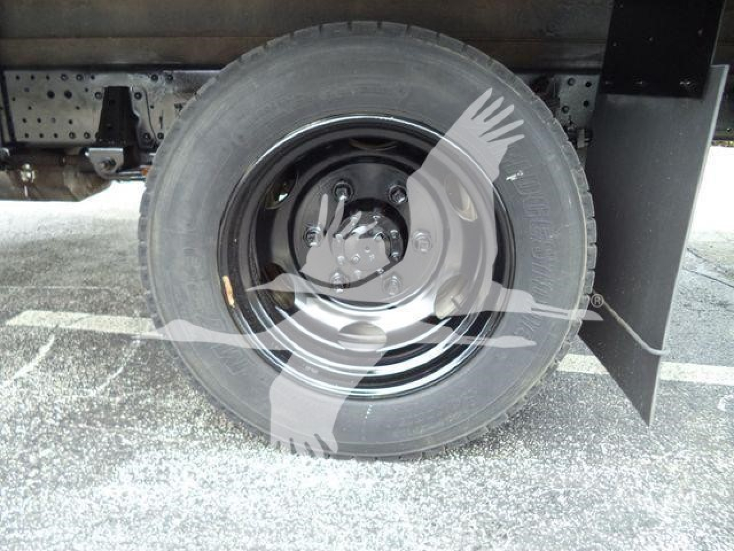 Isuzu NQR wheel and tire visible under refrigerated truck body; spare rim and tire secured; undercarriage components visible.