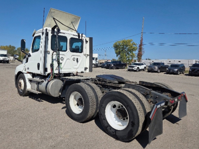 Truck chassis with cab on Freightliner Cascadia 126 axle setup. Visible: dual rear axles, fifth-wheel area, exhaust stack, white wheels, cab with raised roof.