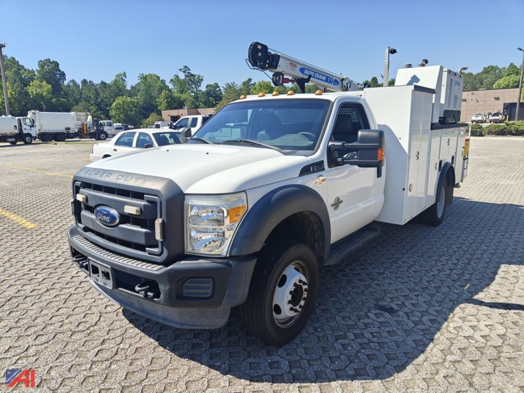 Ford F-550 Super Duty crane truck in service view with mounted crane on bed, front grille and headlights visible, white cab, utility body, daytime outdoor lot.