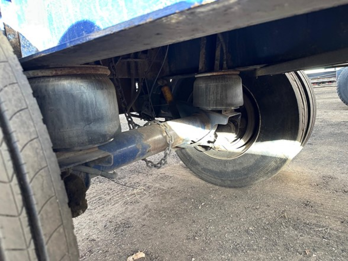 Trailer undercarriage showing suspension and axle components with a blue frame and dual wheels in view.
