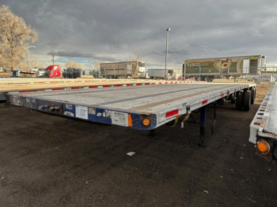 Flatbed trailer in a yard showing long aluminum deck with multiple axles and reflective tape along sides.