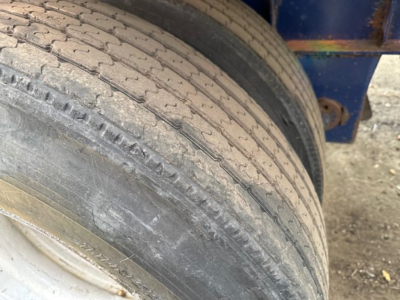 Trailer wheel/tire close-up showing tread and sidewall on Fontaine Infinity flatbed trailer, with blue frame in background.