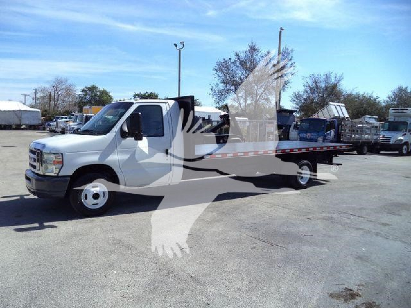 Ford E450 flatbed tow truck in a used lot showing side view with extended bed and white cab.