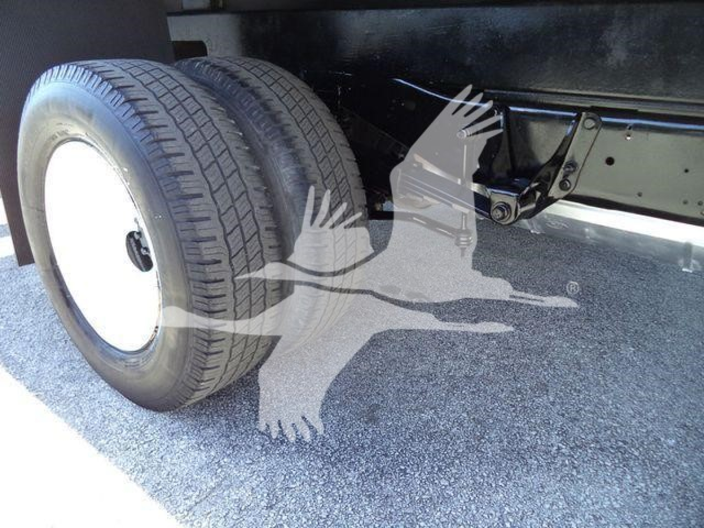 Ford E-450 chassis showing dual rear wheels and flatbed undercarriage; visible components include tire, wheel, frame rails, and suspension elements.