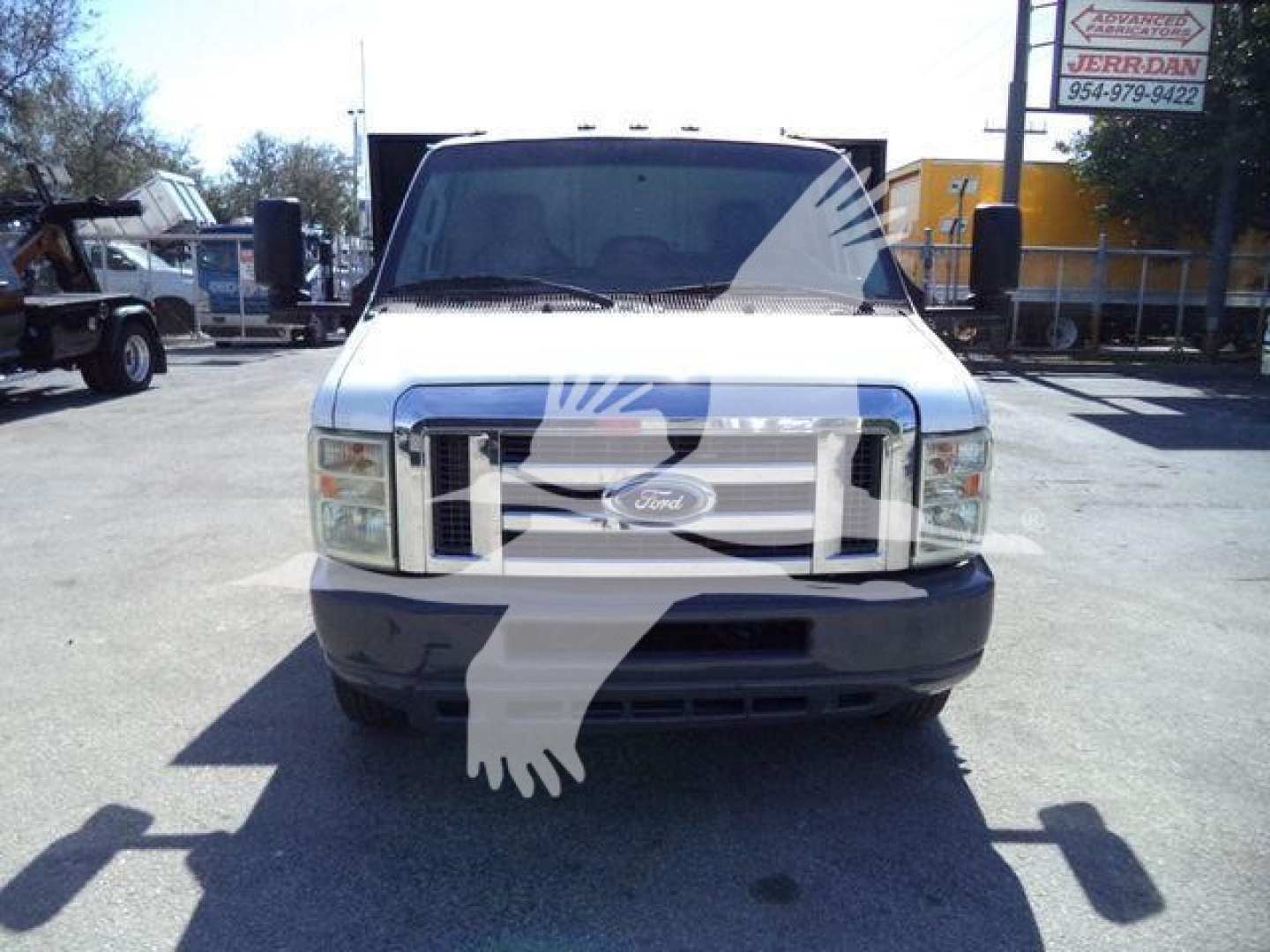 Ford E-450 van front view showing chrome grille with Ford emblem and bumper; headlights visible; windshield and side mirrors; faint reflection of dealership.