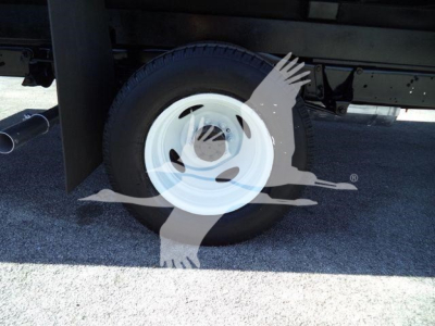 Ford E-450 flatbed truck rear wheel and undercarriage showing white wheel, black tire, and chassis components.