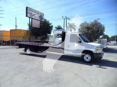 Flatbed tow truck on a sunny lot showing a long wheelbase with white cab and gray flatbed.