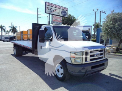 Flatbed tow truck front view showing white cab on a Ford E-450 chassis with flatbed and yellow racks in background.