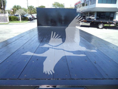 Flatbed truck bed showing a Ford E450 with a dark wooden/metallic bed and a large graphic of a white bird in flight on the surface.