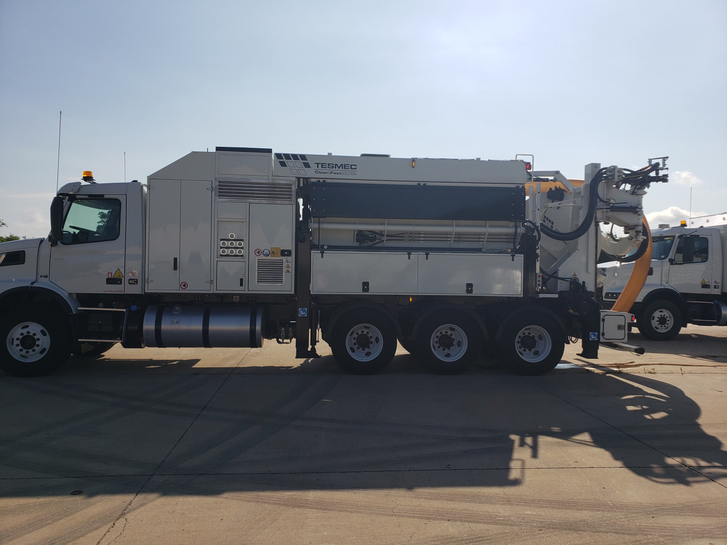 Side view of a large Volvo VHD86B300 vacuum/excavator truck with an attached industrial unit and hose reel; visible text includes DOT safety labels and equipment bays.