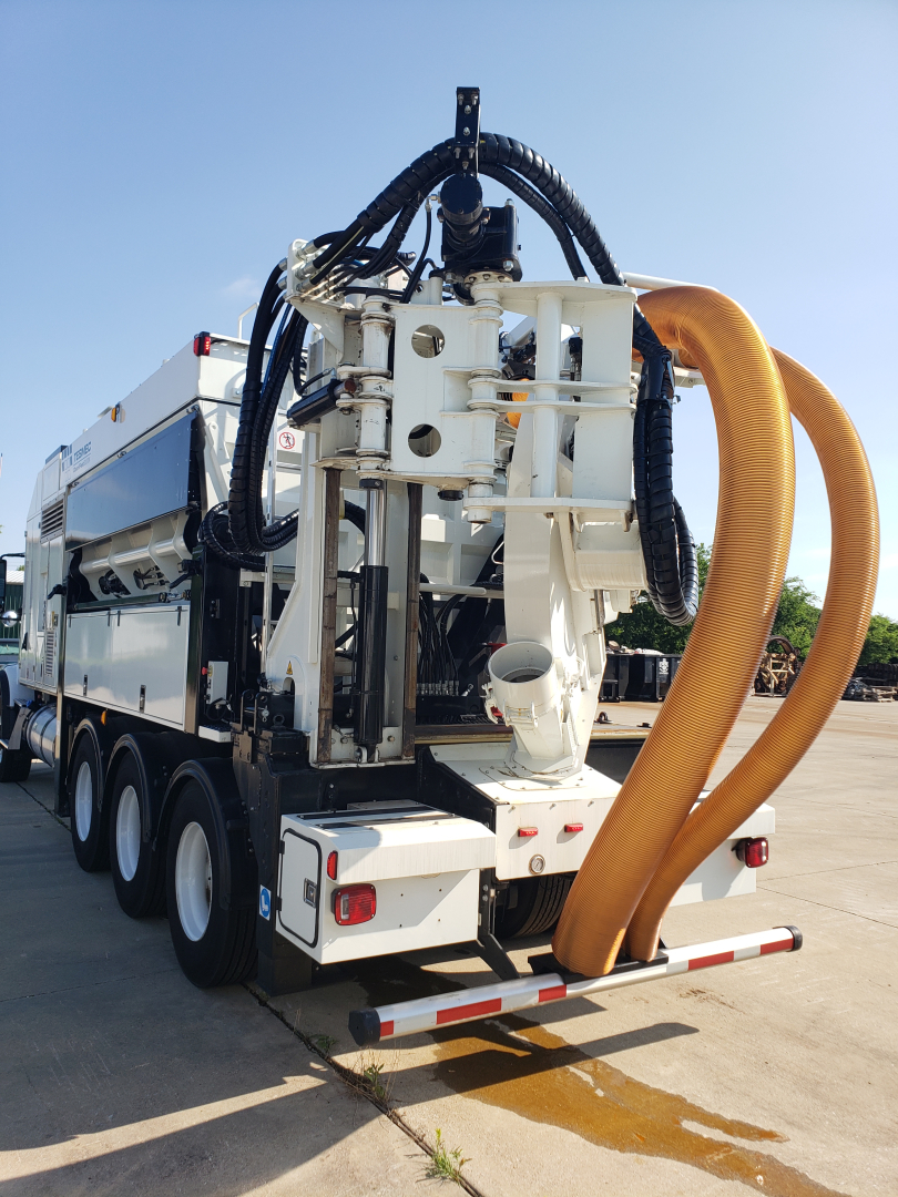Front-left view of a Volvo VHD86B300 sewer line/drain cleaning truck with large orange vacuum hose and rear-mounted equipment, multiple axles, white body, hydraulic lines.